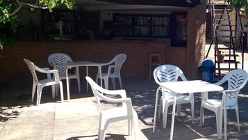 Outdoor seating with white plastic chairs and tables, a brick wall, and a ladder leading to an upper level.