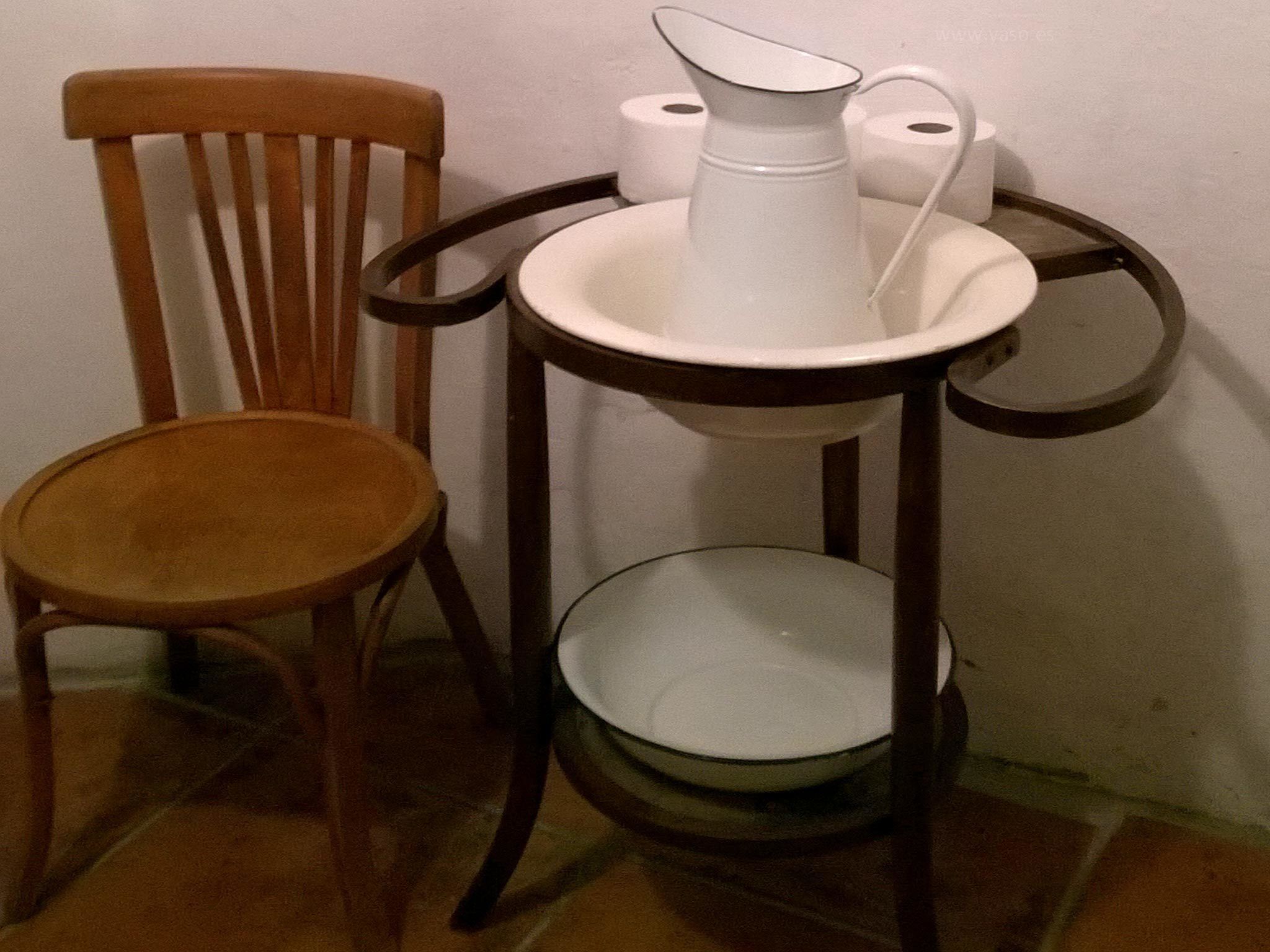 Una mesita con una jarrón, dos rollos de papel higiénico y una silla.