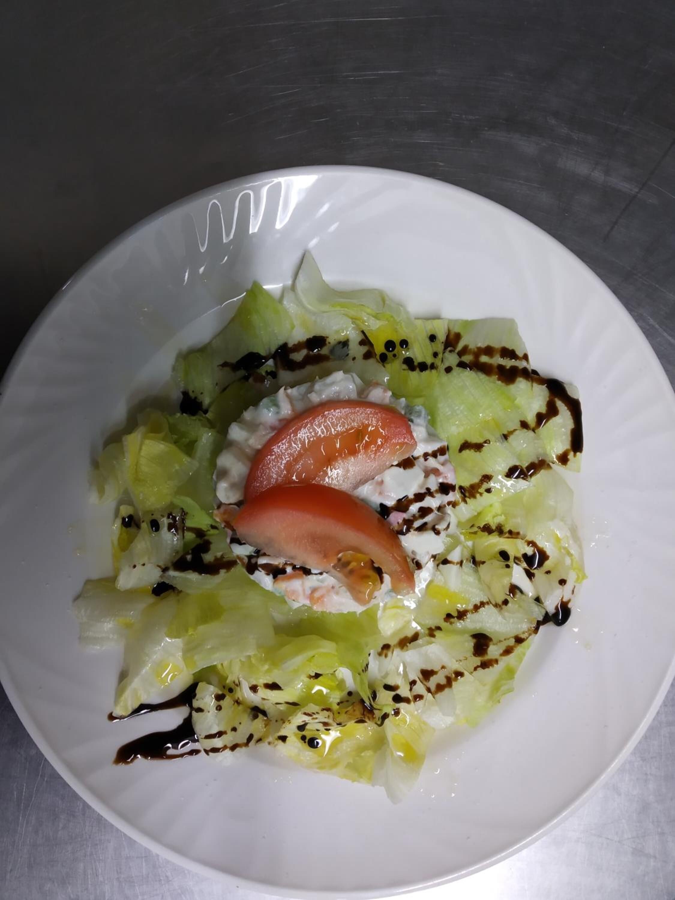Een witte schaal met een salade van sla, tomaat en mogelijk komkommer, met een dressing.