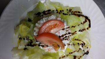 Een witte schaal met een salade van sla, tomaat en mogelijk komkommer, met een dressing.