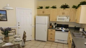 A kitchen with a refrigerator, stove, microwave, and cabinets. There is a dining table with chairs and a potted plant.