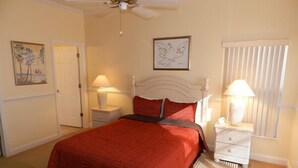 A bedroom with a bed, a nightstand, a lamp, a ceiling fan, a door, and a window with blinds.