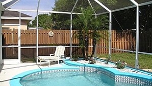 A backyard with a swimming pool, a covered patio area, and a wooden fence.