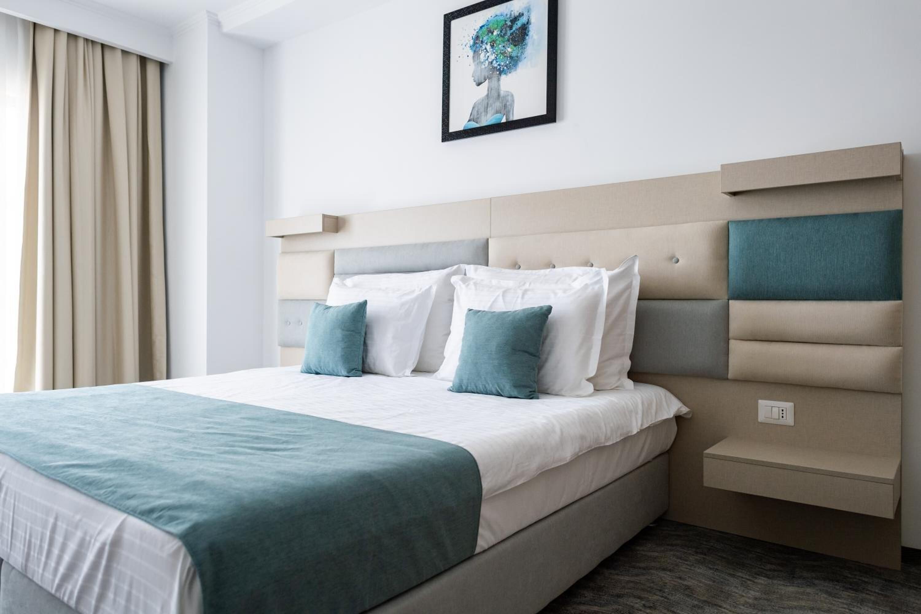 Una habitación de hotel moderna con una cama grande, cabecero con compartimentos de almacenamiento y una obra de arte enmarcada en la pared.