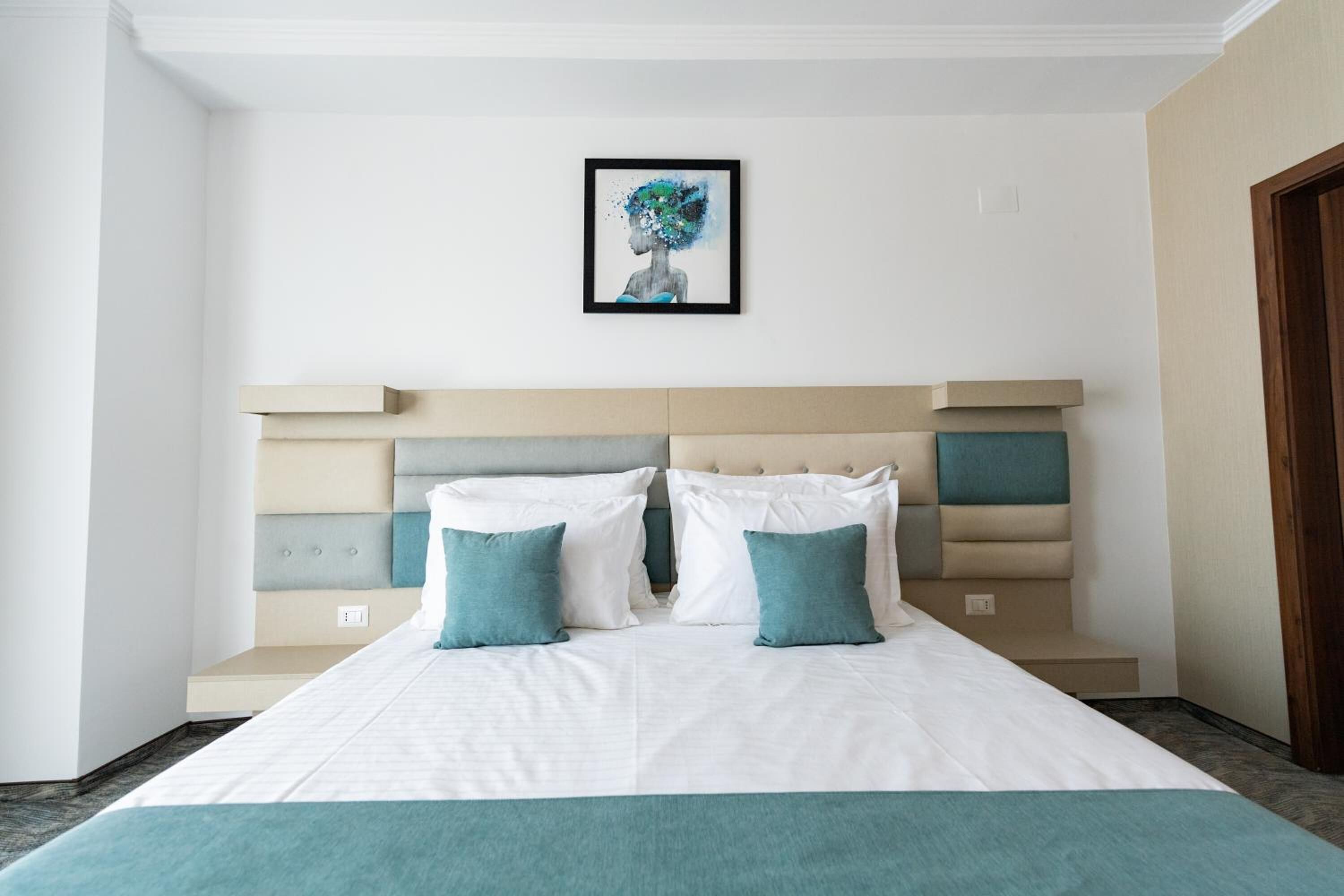 A neatly made bed with a white and teal bedspread, two teal pillows, and a headboard with a geometric design.