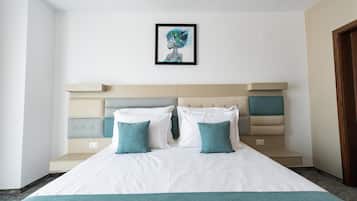 A neatly made bed with a white and teal bedspread, two teal pillows, and a headboard with a geometric design.