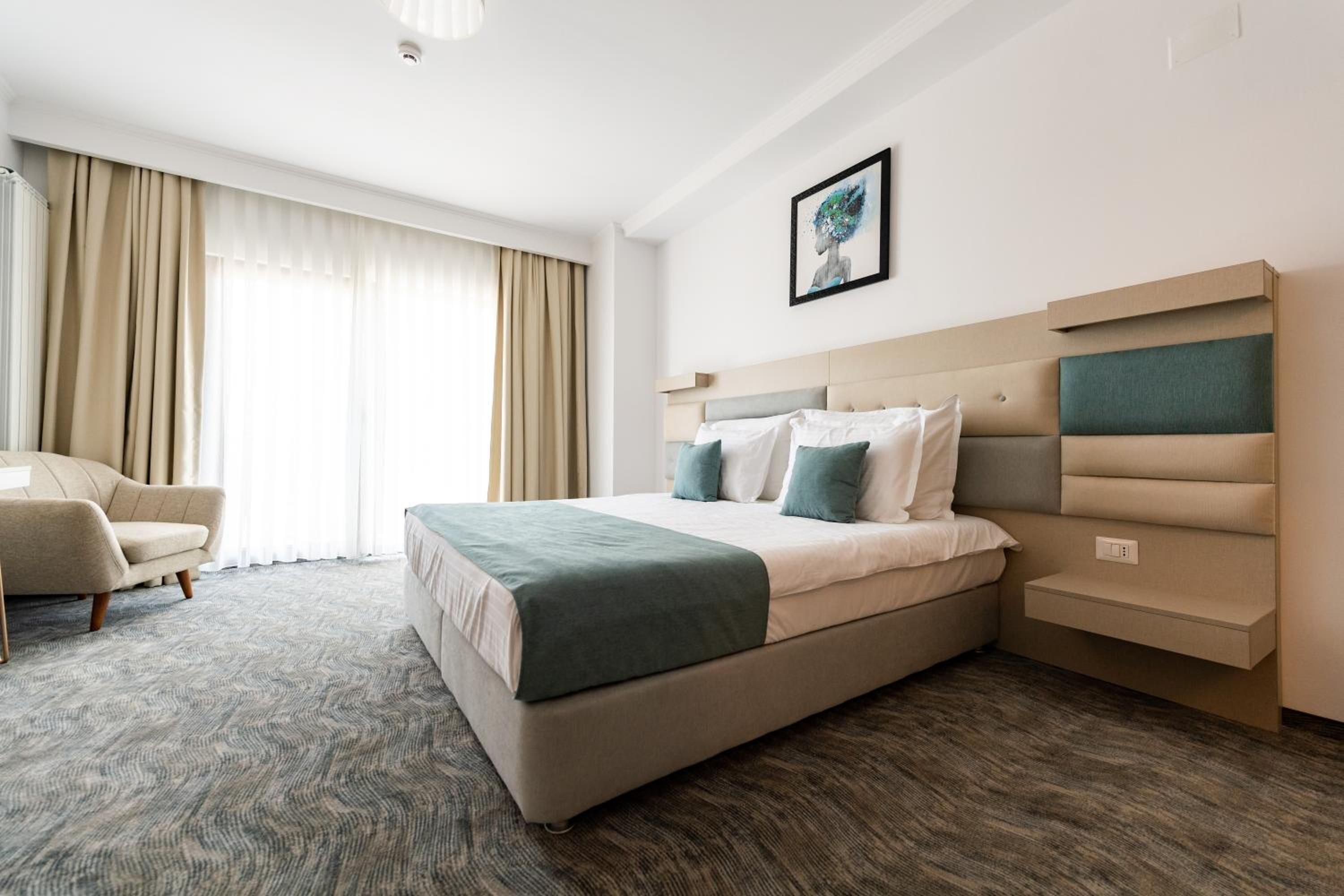 Habitación de hotel con una cama grande, una silla, un cabecero con espacios de almacenamiento y un cuadro en la pared.