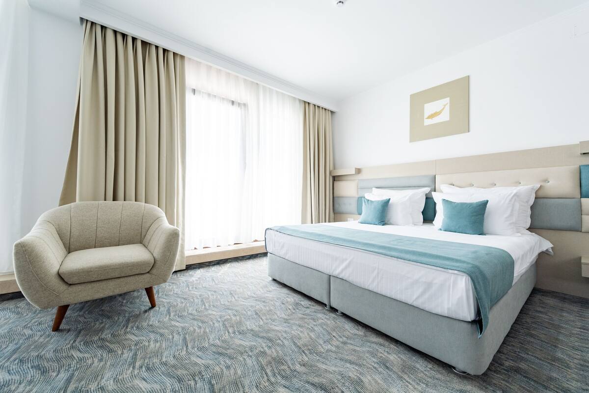 Habitació d'hotel amb un llit, una cadira i una finestra gran amb cortines.
