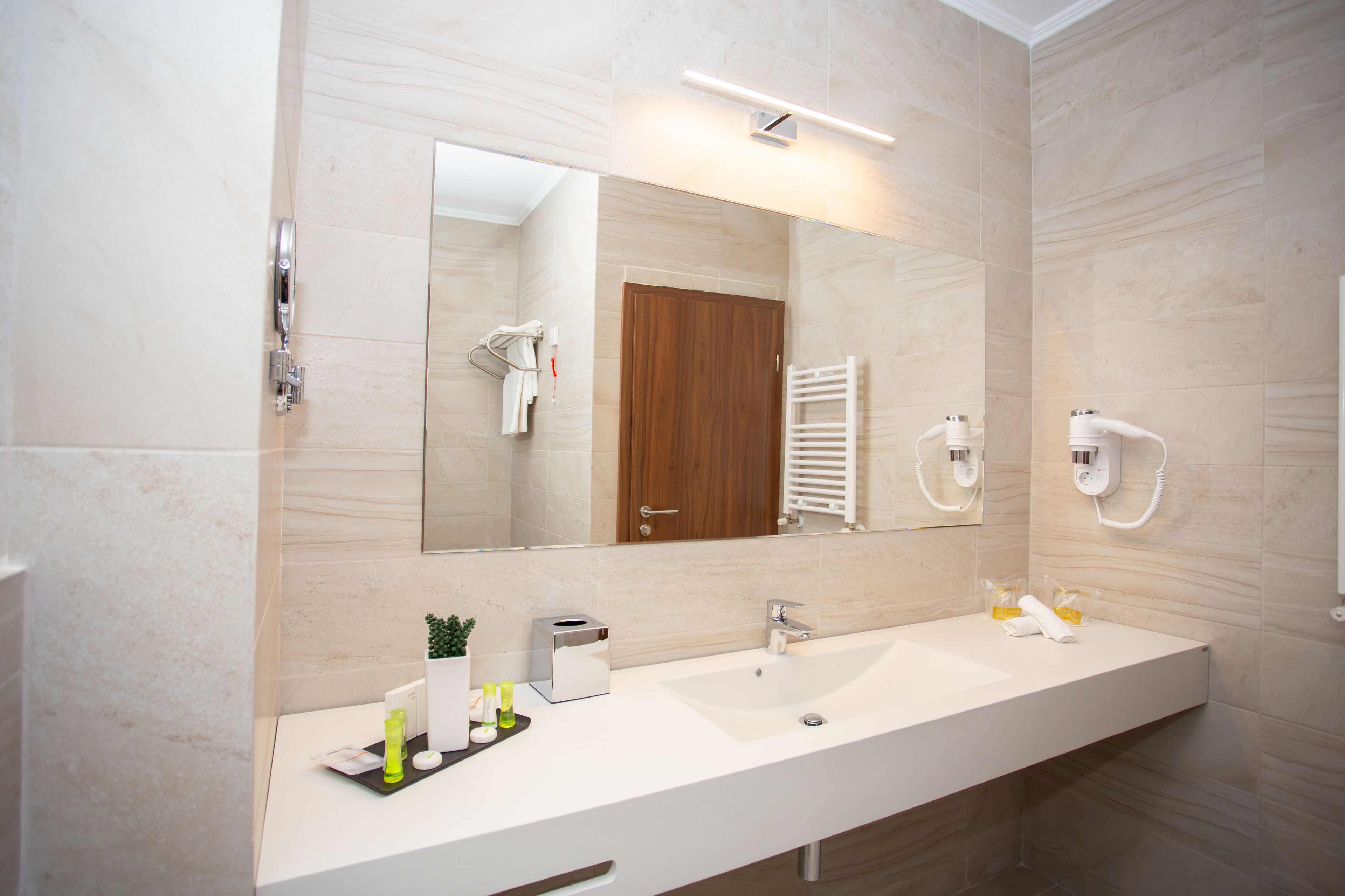 A modern bathroom with a large mirror, two sinks, a towel rack, and a hand dryer.