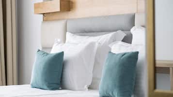 A neatly made bed with white and teal pillows, a wooden headboard, and a light-colored wall.