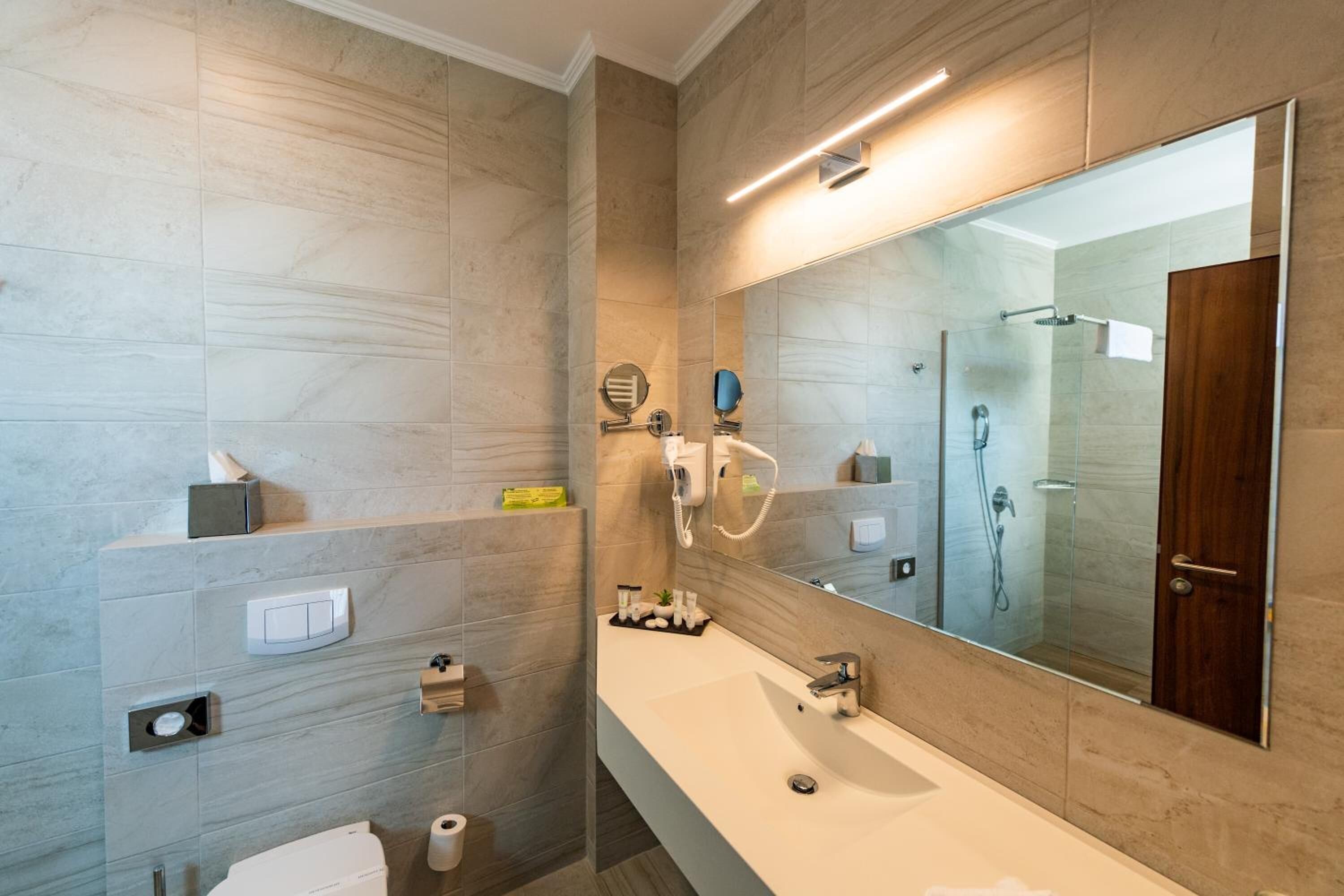 A modern bathroom with a large mirror, a long sink, and a glass shower enclosure.