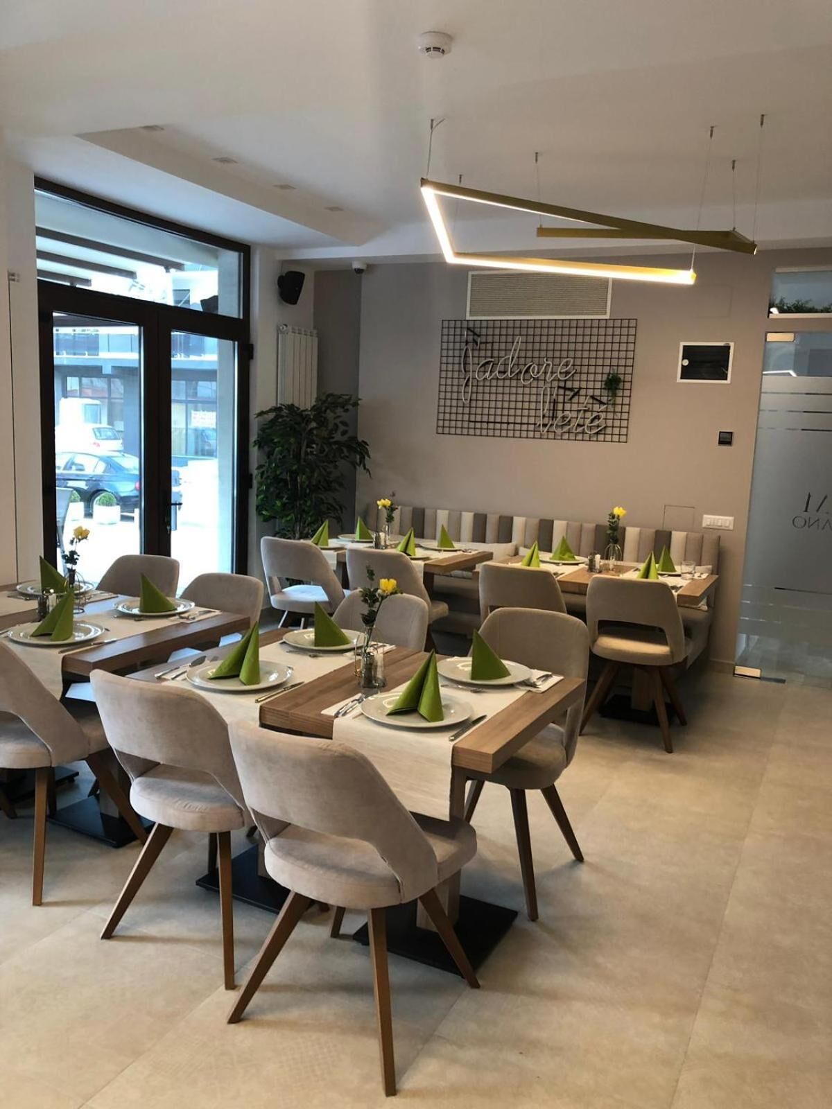 Un comedor moderno con varias mesas y sillas, un ventanal con vista a la calle y un elemento decorativo en la pared.