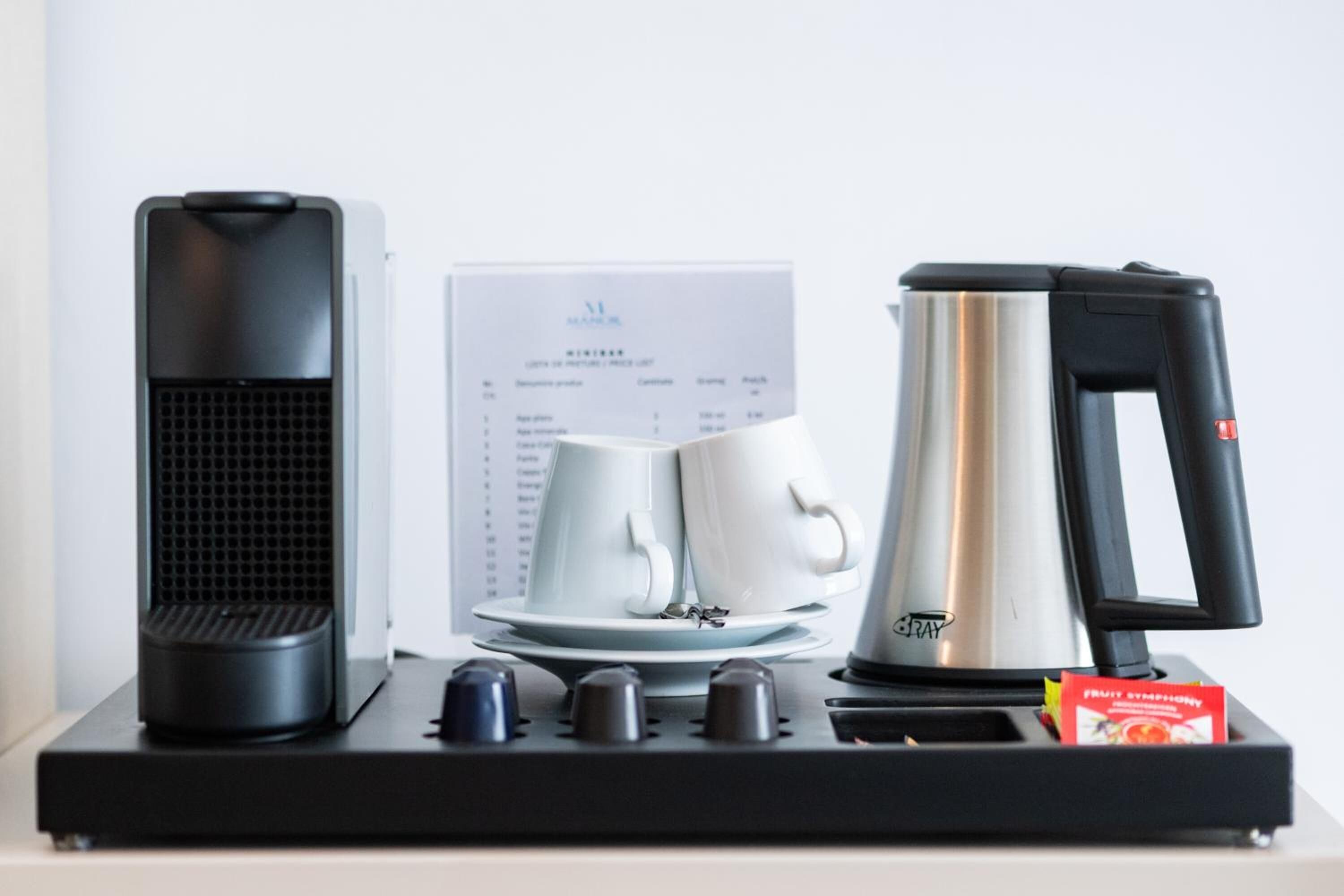 Une machine à café, une bouilloire et un plateau avec deux tasses et sous-tasses blanches, le tout posé sur un plateau noir.