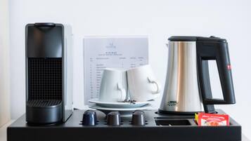 Une machine à café, une bouilloire et un plateau avec deux tasses et sous-tasses blanches, le tout posé sur un plateau noir.