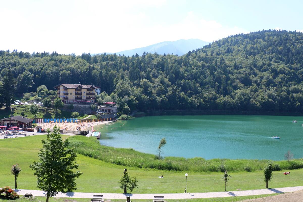 A lakeside hotel with a pool, outdoor seating, and a view of the lake and mountains.