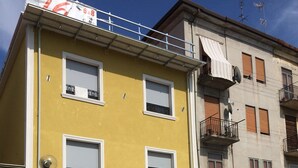 A yellow building with a white awning, a blue car parked in front, and a white fence with potted plants. - B&B Al 16 (Legnago)