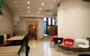 A modern restaurant with wooden tables and chairs, a staircase leading to a lower level, and a view of the outside through large windows. - B&B Al 16 (Legnago)