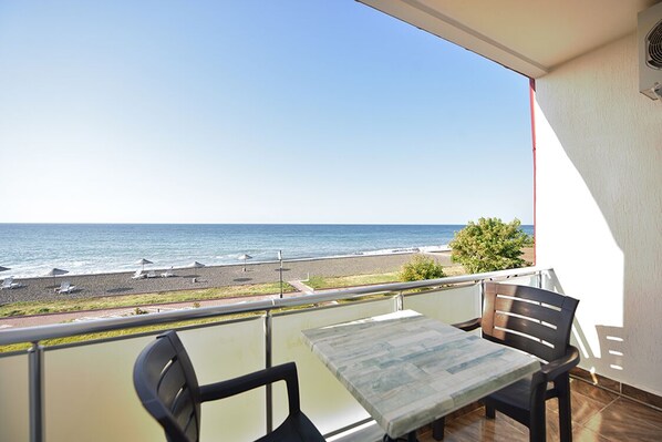 Un balcón con mesa y sillas da a una playa con sombrillas y un camino.