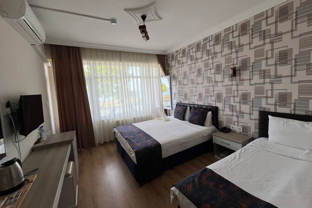 Une chambre d’hôtel avec un lit, un bureau avec un ordinateur, une chaise et une fenêtre avec des rideaux.