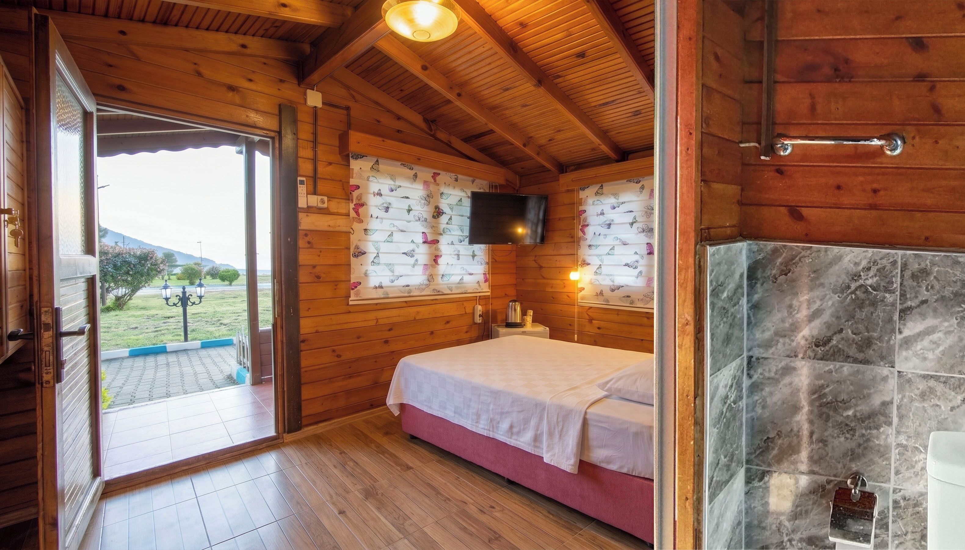 Dormitorio de cabaña de madera con cama, televisión montada en la pared, chimenea y vistas al exterior.