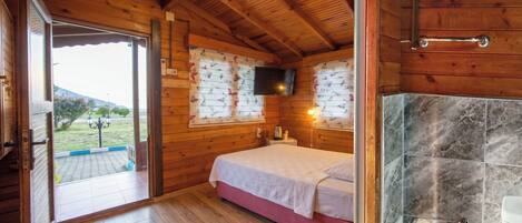 Dormitorio de cabaña de madera con cama, televisión montada en la pared, chimenea y vistas al exterior.