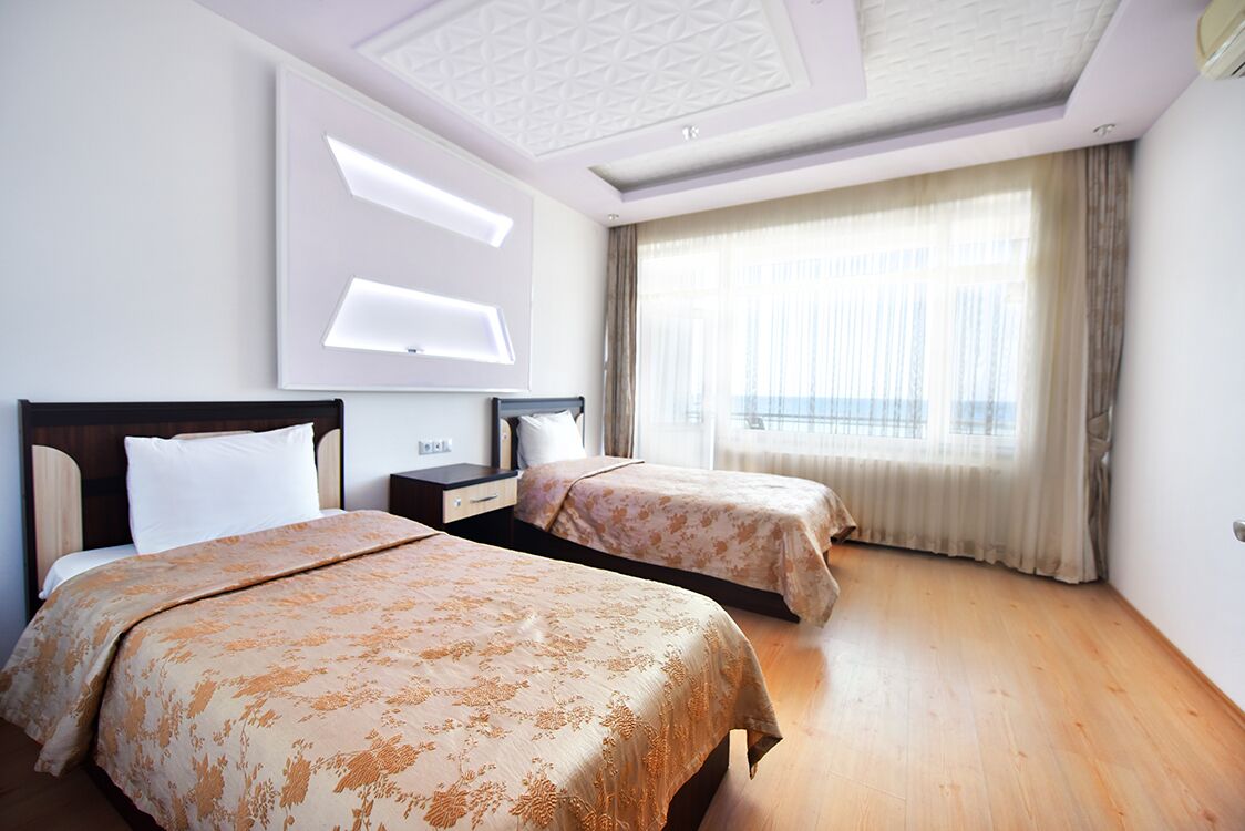 Ein Hotelzimmer mit zwei Betten, einem großen Fenster mit Vorhängen und einem modernen Deckenstil.