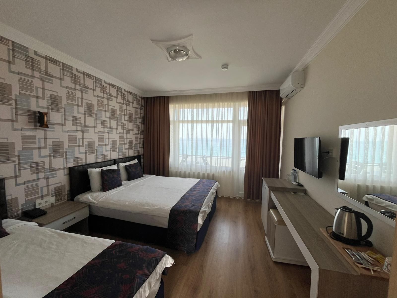 Habitación de hotel con dos camas, un escritorio con televisor, una tetera y una ventana con cortinas.