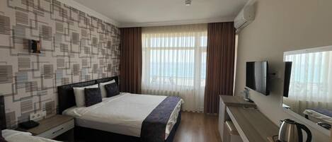 Habitación de hotel con dos camas, un escritorio con televisor, una tetera y una ventana con cortinas.