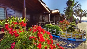 Un edificio con fachada de madera, una valla blanca y flores rojas en primer plano.