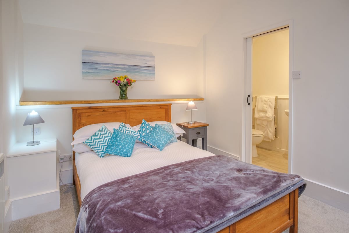 A neatly arranged bedroom with a bed, bedside tables, and a bathroom visible through an open door.