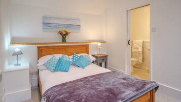A neatly arranged bedroom with a bed, bedside tables, and a bathroom visible through an open door.