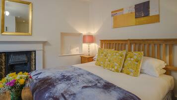 A bedroom with a bed, a mirror, a fireplace, and a wall-mounted artwork.