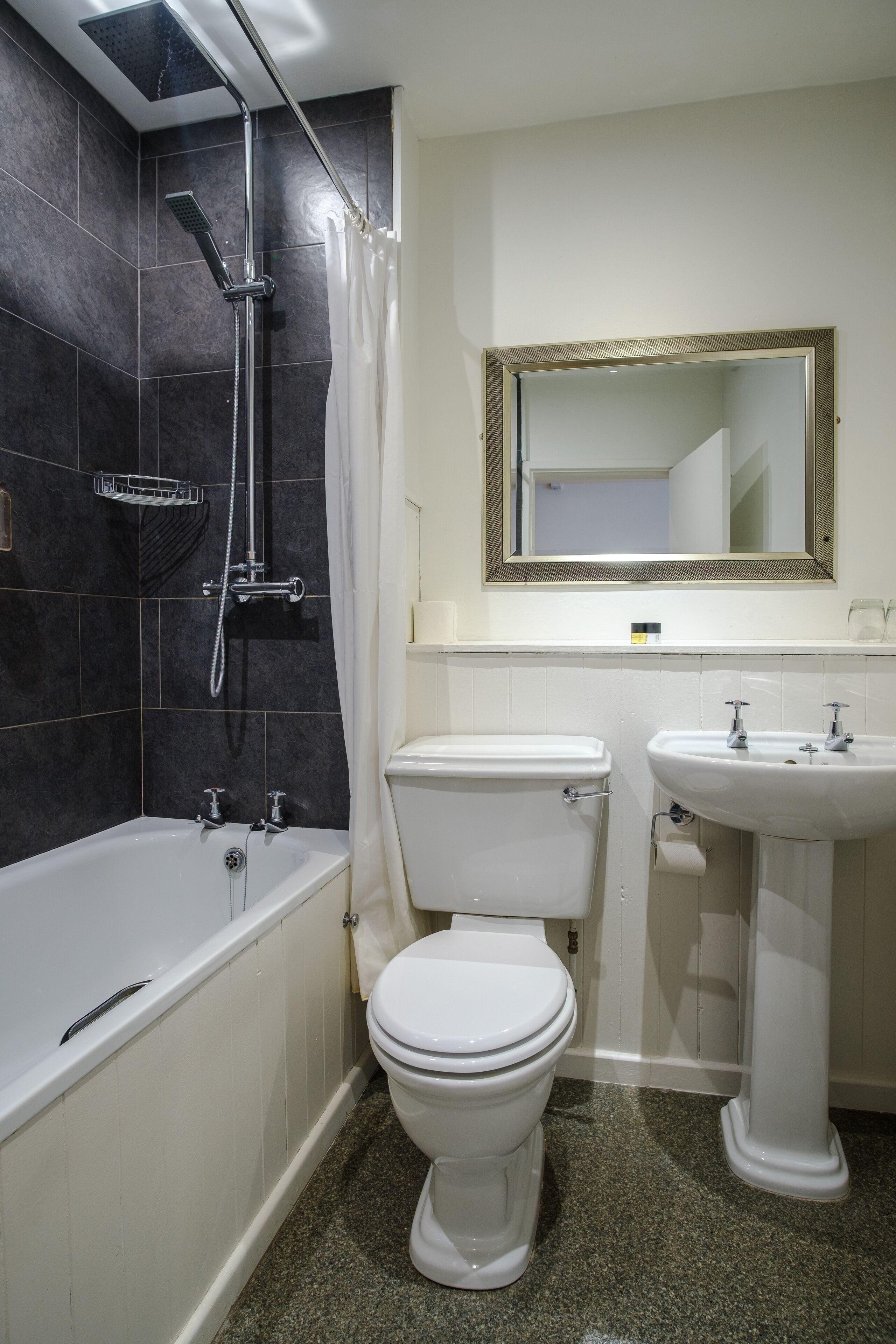 A bathroom with a bathtub, toilet, and sink, with dark tiles on the walls and a mirror above the sink.