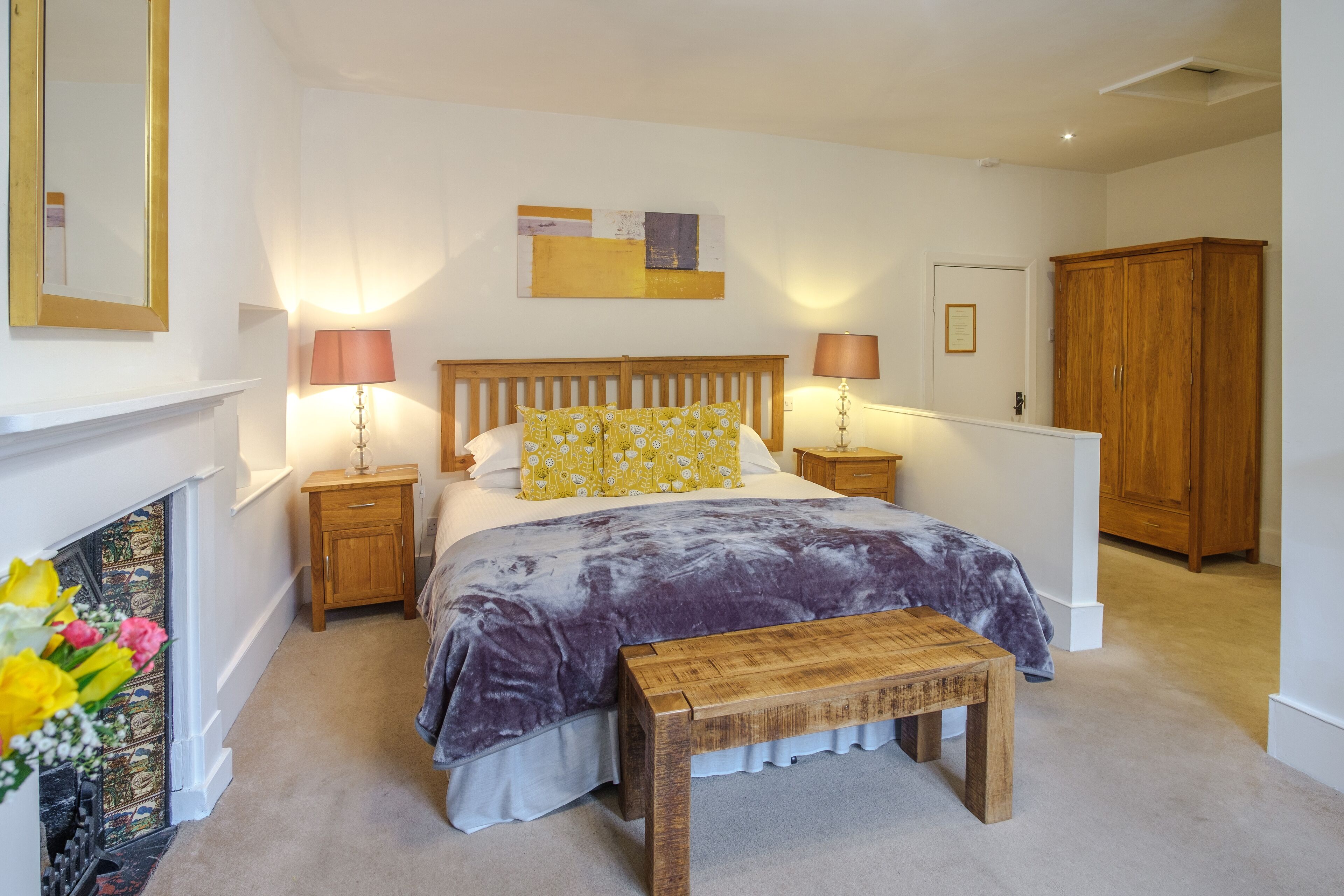 A bedroom with a bed, bedside tables, a wooden bench, a fireplace, and a wardrobe.