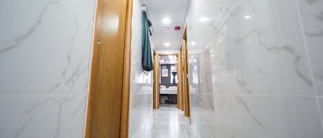 A hallway with marble walls and wooden doors, leading to a room with a bed and a bathroom.