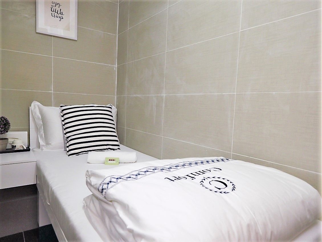 Una cama bien hecha con un almohadón azul y blanco a rayas, un almohadón blanco y una colcha blanca con un monograma.