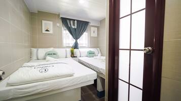 Quarto de hotel com duas camas, uma janela com cortinas, uma porta e um ar condicionado fixado na parede.