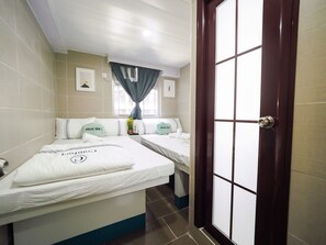 A hotel room with two beds, a window with curtains, a door, and a wall-mounted air conditioning unit. - HK International Hostel (Kowloon)