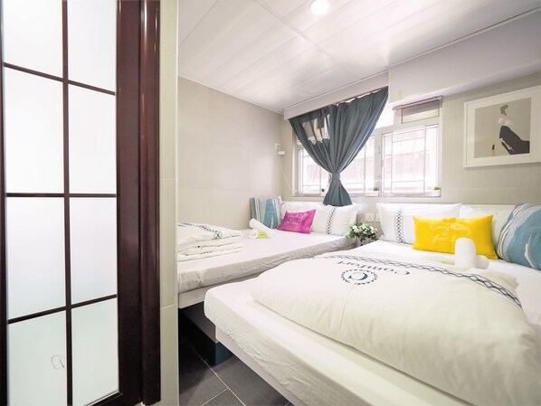 A hotel room with two beds, a window with curtains, a wall-mounted air conditioner, and a framed picture. - HK International Hostel (Kowloon)
