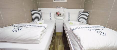 Habitación de hotel con dos camas individuales, un escritorio pequeño con silla, un cuadro enmarcado en la pared y suelo de baldosas.