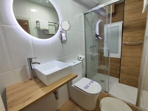 Un baño moderno con un lavamanos, espejo y retrete blancos.
