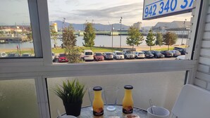 Taula amb sobretaula de vidre, dues ampolles i tres tasses, amb vista a cotxes aparcats i una massa d'aigua al fons.