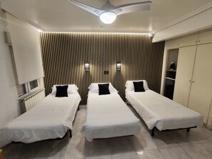 Una habitación de hotel con tres camas individuales, un ventilador de techo, un radiador y un armario.