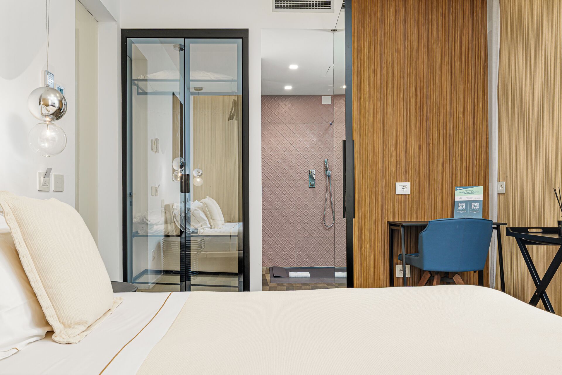 Une chambre d’hôtel équipée d’un lit, d’un bureau, d’une chaise, d’une douche et d’une porte en verre donnant sur la salle de bain.