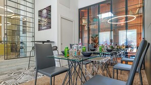 A modern dining area with glass tables and chairs, a large window with a view, and a decorative painting on the wall. - Hotiday Olbia Wallure (Olbia)