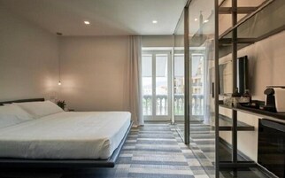 Una habitación de hotel con cama, televisión, balcón y mostrador de recepción.