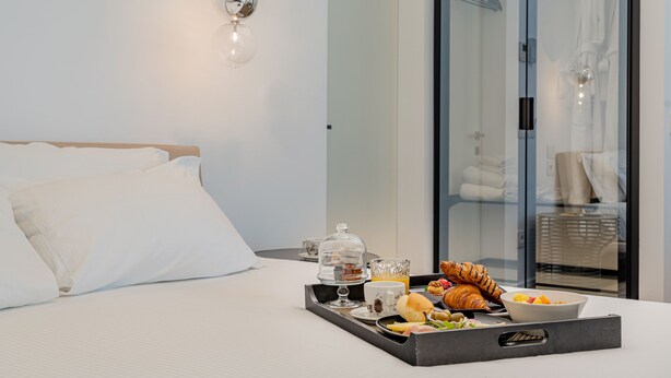 A neatly made bed with white linens, a tray with breakfast items including croissants, a bowl of fruit, and a coffee cup. - Hotiday Olbia Wallure (Olbia)