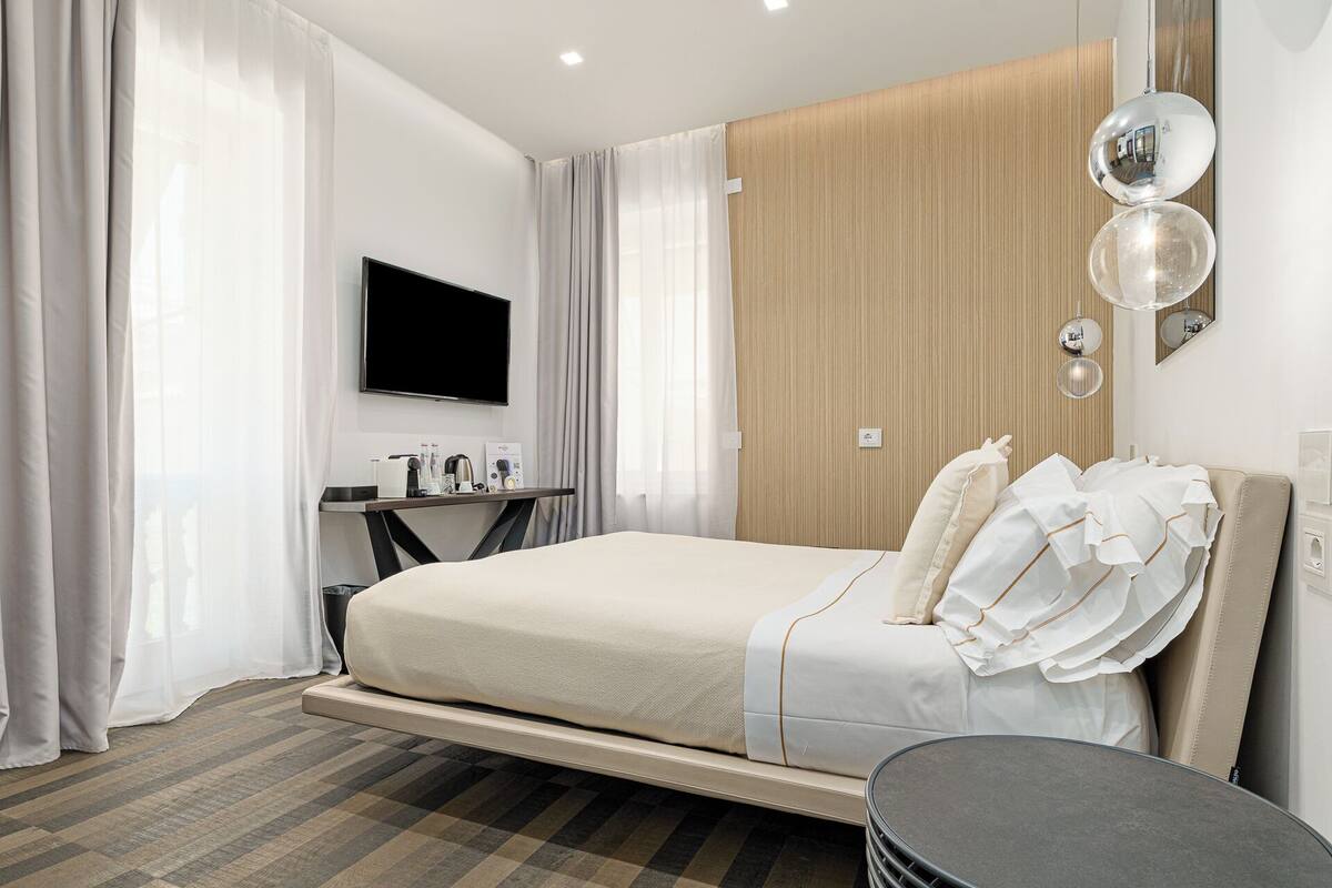 Una habitación de hotel con cama, escritorio, televisor y espejo.