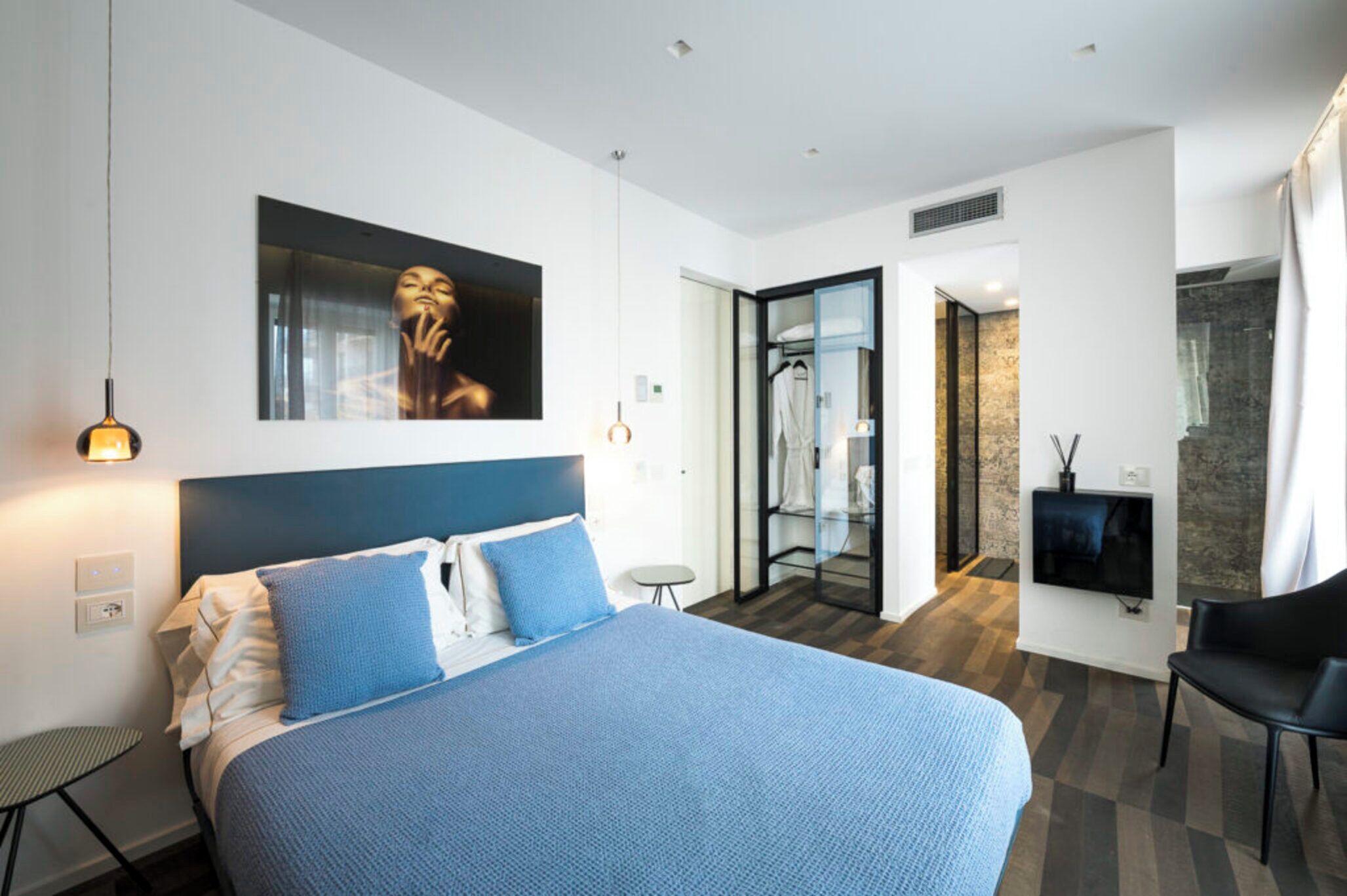 Ein modernes Hotelzimmer mit einem großen Bett, einem Fernseher, einer Sitzecke und einem durch eine offene Tür einsehbaren Badezimmer.
