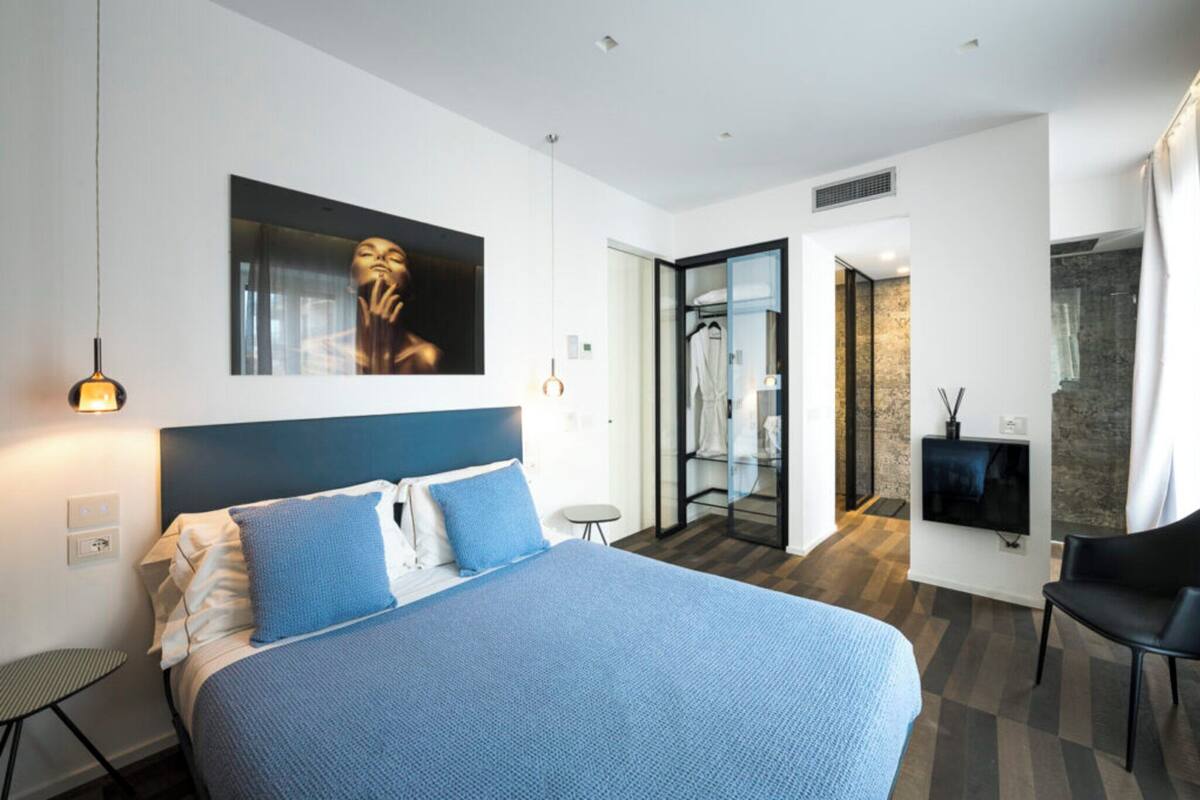 Una habitación de hotel moderna con una cama grande, televisión, zona de estar y baño visible a través de una puerta abierta.